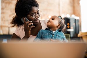 Smiling young woman looking at cute newborn daughter while having phone conversation stock photo