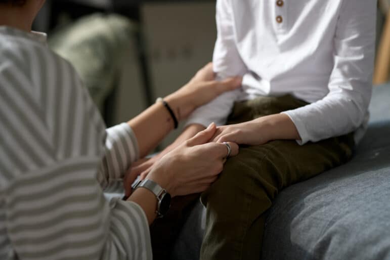 Close-up of mother supporting her little son holding his hands while they sitting and talking in the room