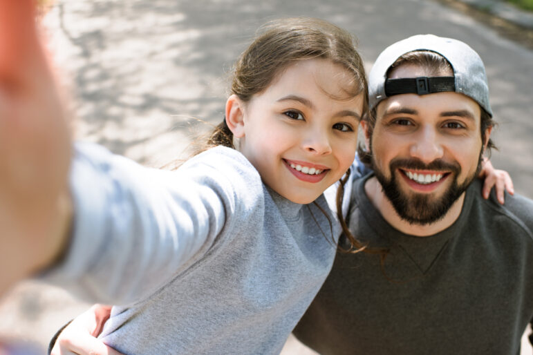 Daughter taking selfie smiling with father in a park.