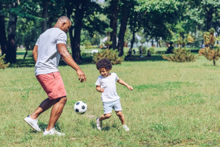 African American father playing football with young son in park