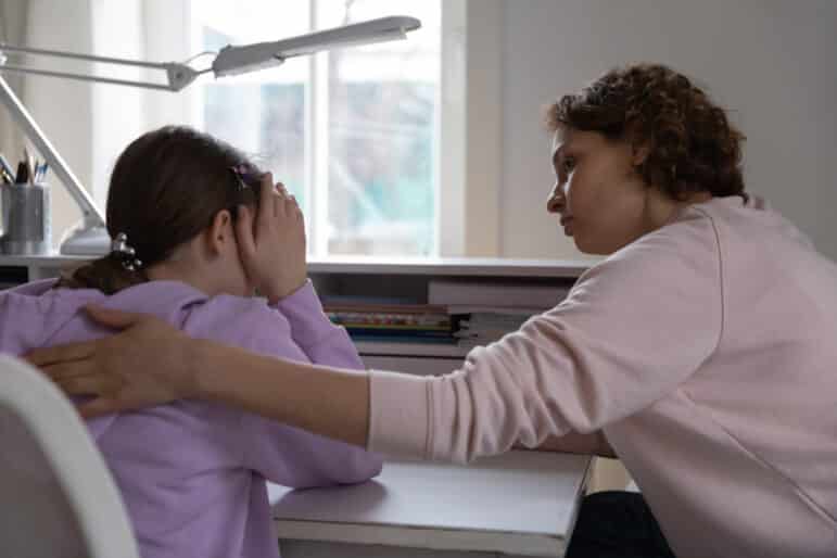 Worried young mother talking comforting upset teen daughter apologizing at home.