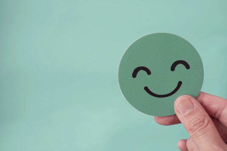 Fingers holding green happy smile face paper cut
